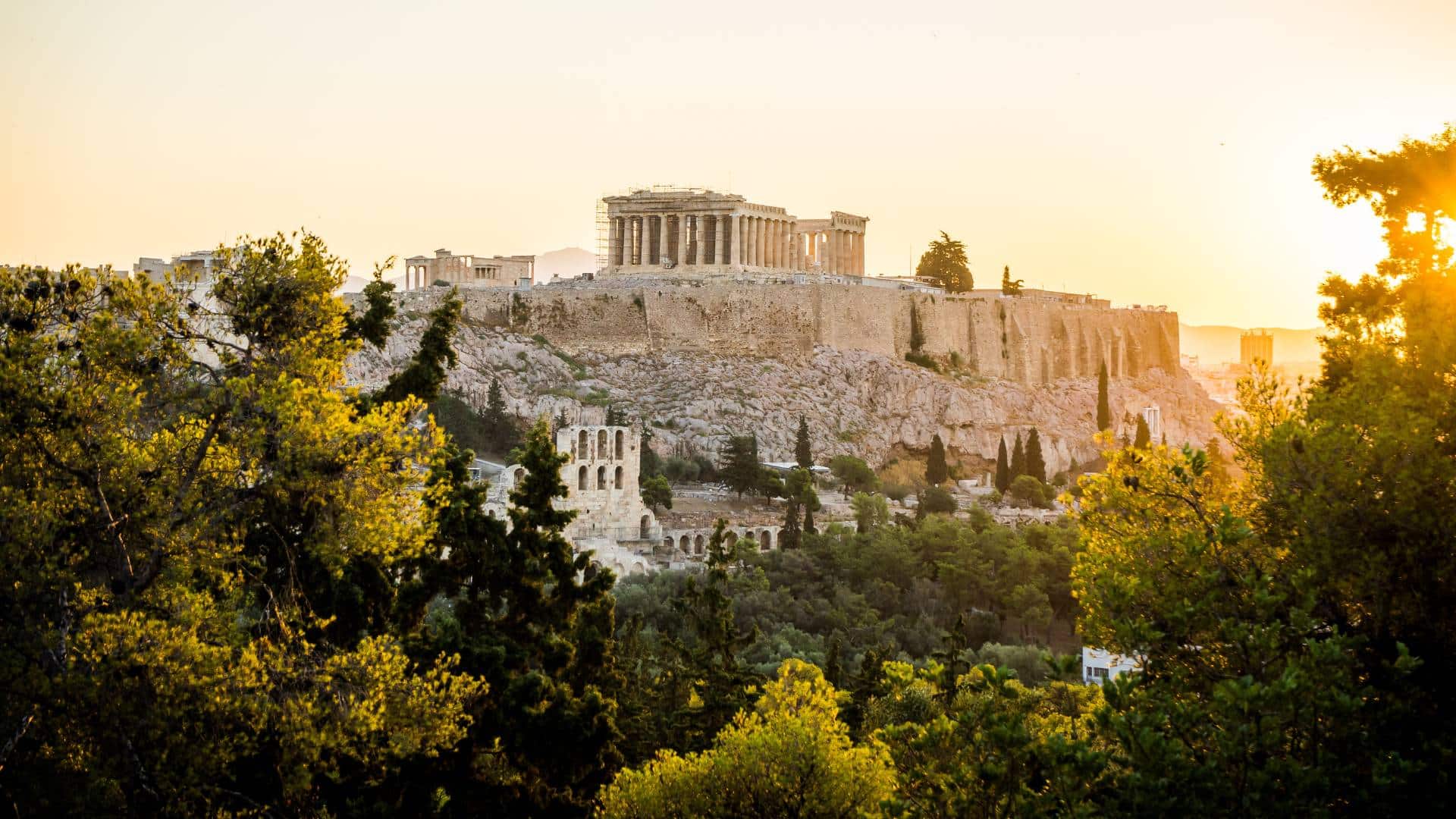 Historical site greece. Best travel agency in Greece View of the Acropolis in Athens at sunset, where the Parthenon majestically crowns the rocky hill, part of Greece's rich tapestry of historical sites, surrounded by lush greenery. Offbeat-Travel